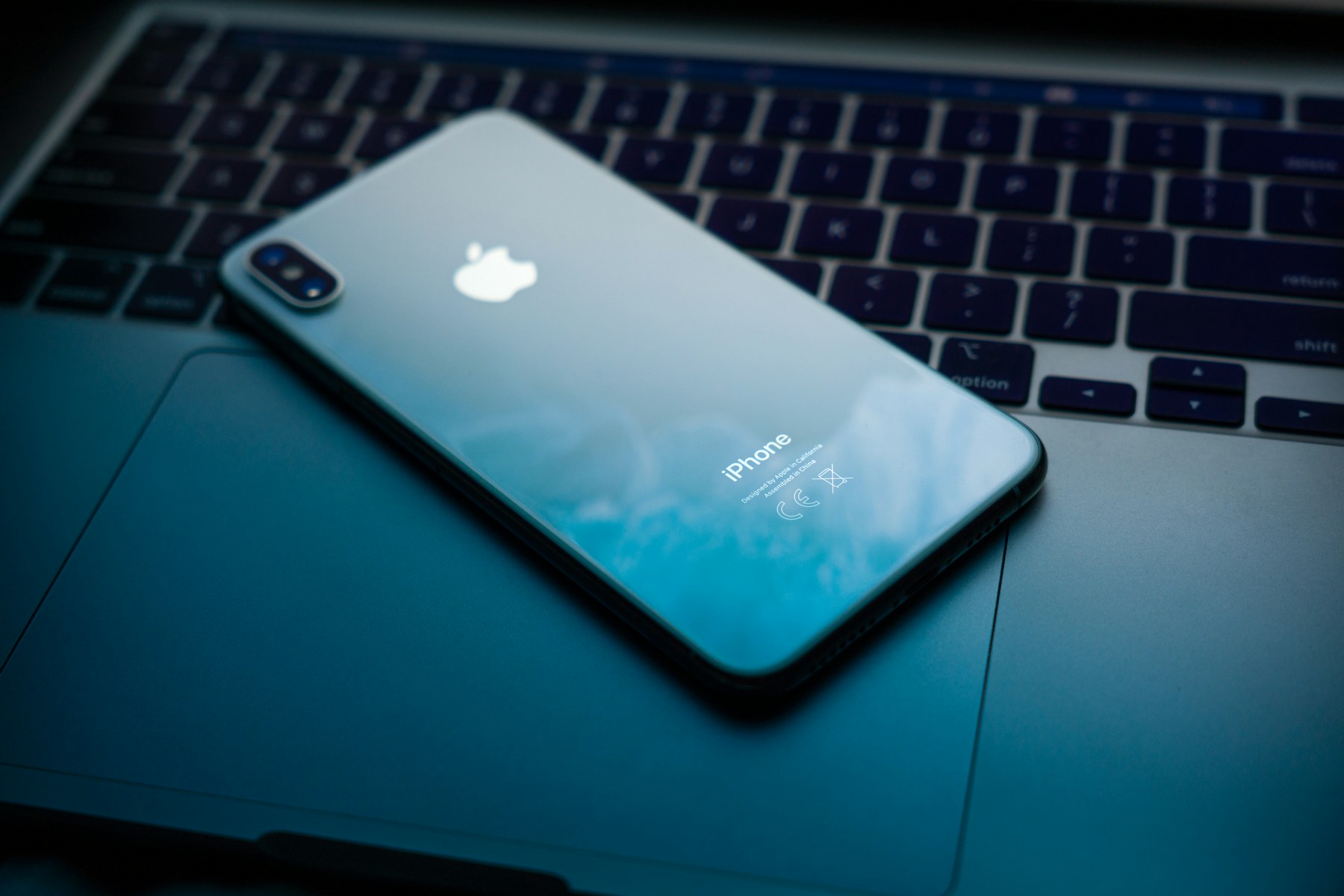 An iPhone resting on a laptop in a dark blue workspace
